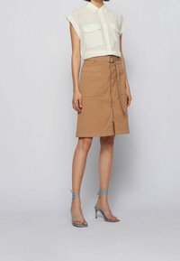 Rok katun beige dengan ritsleting depan dan dua saku, dipasangkan dengan kemeja lengan panjang tipis dan sandal hak tinggi berpengikat biru.