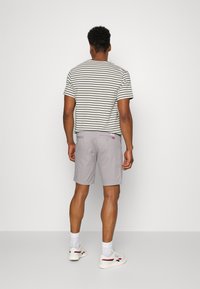 Stribet kortærmet skjorte i grå og hvid, parret med lysegrå shorts. Hvide sneakers med røde og marineblå accenter. Enkel design generelt.