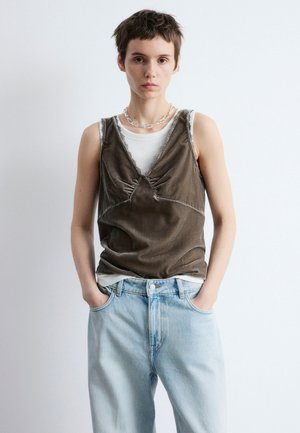Olive green sleeveless top with gathered detail, layered over a white ribbed tank. Paired with light blue high-waisted jeans.