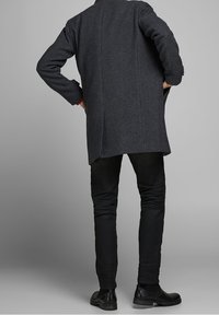 Mörkgrå, strukturerad rock med rak skärning, som har långa ärmar och ett ryggslits, ihop med svarta slim-fit byxor och skor.