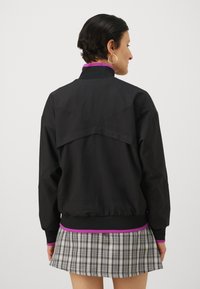 Black bomber jacket with a relaxed fit, featuring a contrasting purple collar and hem, and an oversized back panel design.