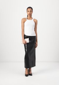 Witte mouwloze tanktop, zwarte leren maxi rok en zwarte hakken, houdend een gestructureerde romige clutch. Soepele stof en slank ontwerp.