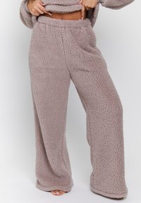 Pantalones de pierna ancha, difusos y marrones claros, con cintura elástica, bolsillos laterales y una textura suave que proporcionan comodidad y calidez.
