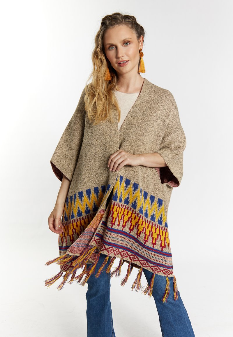 Poncho maro țesut cu un model geometric colorat la margine, având detalii cu franjuri. Stil kimono, cu mâneci largi.