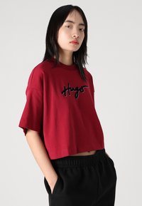 Rode cropped t-shirt van katoen met korte mouwen, voorzien van zwart geborduurde tekst "Hugo" op de voorkant. Gecombineerd met zwarte sweatpants.
