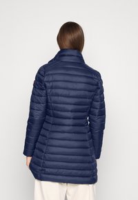 Laivastonsininen puhvitakki korkealla kauluksella, vaakasuoralla tikkauksella ja muotoonommellulla siluetilla. Takissa on pitkät hihat ja keskipitkä muoto.