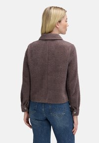 Kort, fuzzy brun jakke med krave, knapmanchetter og cropped design, parret med høj talje blå jeans. Tekstureret materiale synligt.