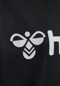 Der schwarze Stoff zeigt eine weiße Grafik einer stilisierten Biene mit abgerundeten Flügeln und Chevron-Mustern darunter. Einfaches und auffälliges Design.