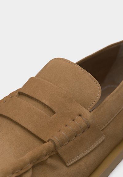 Mocassin en daim marron clair avec une bride sur le dessus et des coutures détaillées le long de l'avant et des côtés.