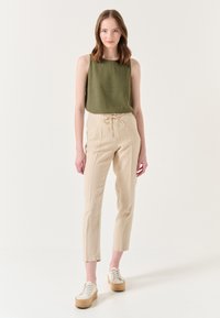 Grünes ärmelloses Top, beigefarbene kordelzug Hosen und weiße Plateausneaker. Leichter Stoff, gerade Beinform und neutrale Farben.