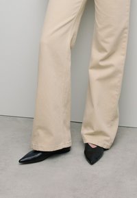 Beige wijde broek met een soepel textuur, gecombineerd met zwarte puntige flats met een leren afwerking en een minimalistisch ontwerp.