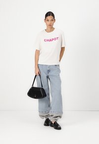 Balta marškinėliai su rožiniu užrašu "CHAPOT", šviesiai mėlynos plačios kelnės, juoda rankinė ir juodi batai su tekstūruotu raštu.