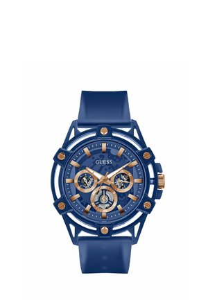 Blue Guess wristwatch with gold-tone hour markers, three subdials, skeleton dial sections, and a blue silicone strap.