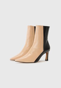 Bottines en cuir avec un embout pointu, présentant un devant beige et un dos noir contrastant, montées sur un talon fin. Texture lisse sur l'ensemble.