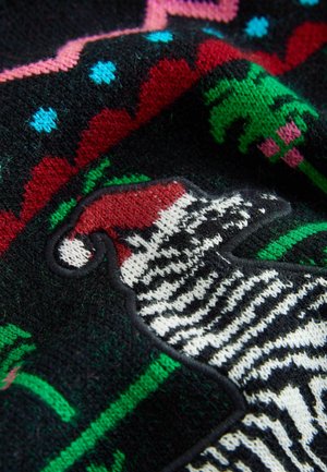 Pletený svetr má černý základ s barevnými geometrickými vzory, včetně červené, zelené a modré. Výrazný design zebry v bílé a černé barvě.