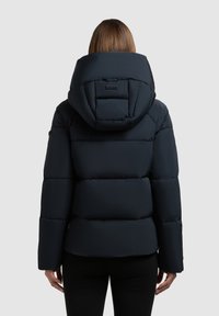 Giubbotto imbottito blu navy con cappuccio grande, design trapuntato e polsini elasticizzati. Texture liscia e lunghezza leggermente accorciata sul retro.