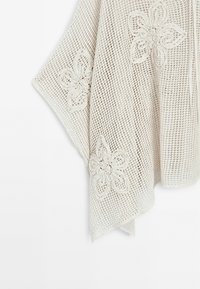 Beżowa tkanina o otwartym splocie z haftowanymi wzorami kwiatowymi, przedstawiająca zbliżenie na wygiętą tkanię z teksturowymi detalami.