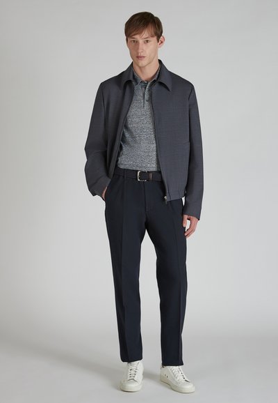 Ciemnoszara rozpinana kurtka na niebieskiej teksturowanej koszuli, w zestawieniu z granatowymi spodniami i białymi trampkami, z plecionym czarnym paskiem.