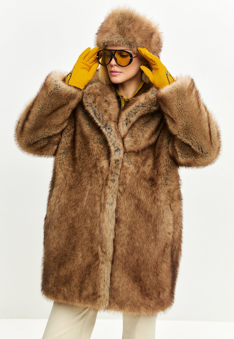 Brun faux fur frakke med bred krave, matchende pels hat og gule handsker. Frakken har en blød tekstur og en løs, oversized pasform.