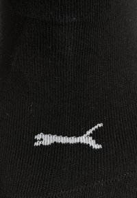 Tessuto nero con un piccolo logo Puma bianco ricamato, che mostra un puma in salto su una superficie a maglia testurizzata.