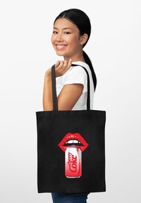 Borsa tote nera con una grafica di labbra rosse audaci che tiene una lattina di Cherry Coke. Materiale in cotone, con manici resistenti e una texture liscia.