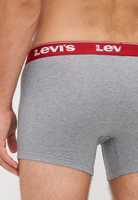 Sive bombažne bokserice z rdečim pasom, ki nosi belo blagovno znamko "Levi's", prikazujejo prilegajoč in gladek dizajn.