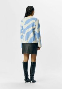 Strikket sweater med et blåt og cremefarvet abstrakt mønster, parret med en sort læderskirt og knæhøje sorte stiletto støvler.