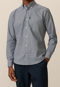 Camicia a maniche lunghe a scacchi blu navy e bianca con colletto a bottoni e taschino sul petto, realizzata in tessuto di cotone intrecciato.