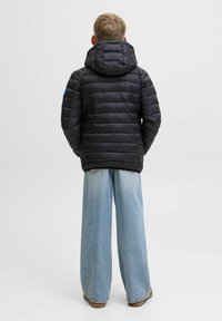 Svart puffjacka med huva, quiltad design och elastiska ärmslut. Bärs över vidbeniga ljusblå jeans och bruna skor.