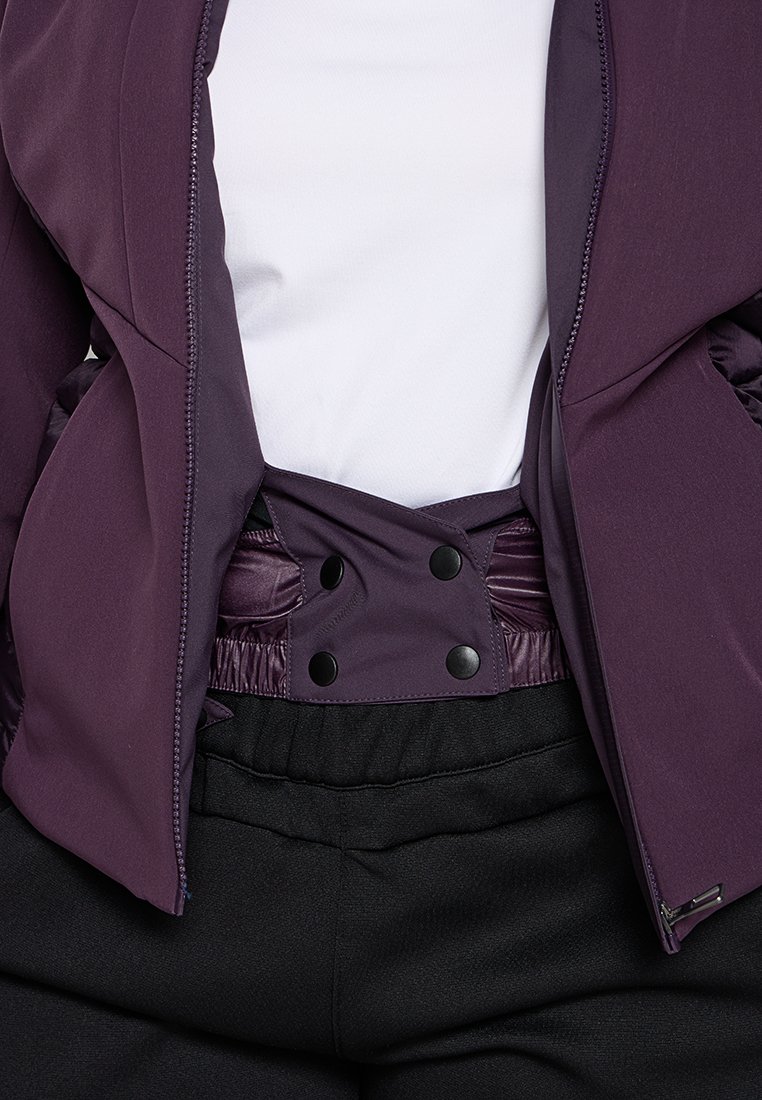 Giacca viola con una texture liscia, dotata di zip anteriore e bottoni a pressione in vita, abbinata a pantaloni neri con cintura elastica.