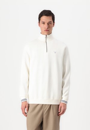White zip-neck pullover with a soft texture, featuring a small logo on the chest and striped accents on the cuffs.