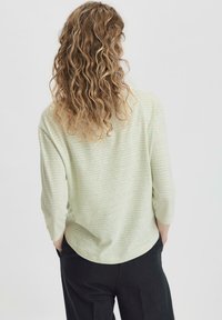 Hellgrüner gestreifter Pullover mit drei Viertelärmel, weicher Textur, lässigem Schnitt und abgerundetem Saum, kombiniert mit dunklen Hosen.