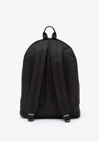 Mochila negra con correas de malla acolchada, forma redondeada y textura suave. Los broches ajustables se encuentran en las correas.
