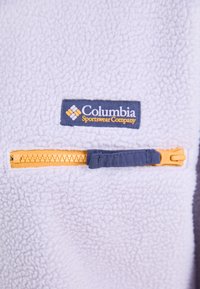Pulover iz flisa v svetlo vijolični barvi z logotipom Columbia Sportswear. Ima oranžni žep z zadrgo in mornarsko modro zadrgo ter teksturirano tkanino.