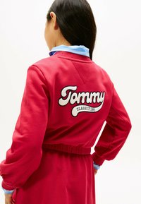 Czerwona sukienka-sweterek z elastycznym paskiem w talii, z białym haftowanym logo "Tommy" i napisem "CLASS OF 1995" na plecach.