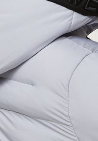 Grauer Stepp-Steppjackenstoff mit gesteppter Struktur, der eine weiche Textur und ein kontrastierendes schwarzes elastisches Band an der Taille aufweist.