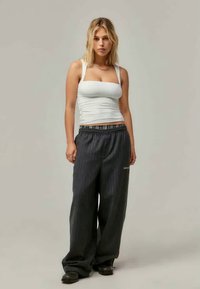 Λευκό εκ fitted tank top συνδυασμένο με χαλαρές, σκούρες ριγέ φόρμες που διαθέτουν ελαστική μέση και λεπτομέρεια με λογότυπο. Μαύρα παπούτσια.