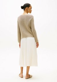 Beiger gehäkelter Pullover mit langen Ärmeln, kombiniert mit einem weißen plissierten Midikleid und beigen flachen Sandalen. Schlichtes und minimalistisches Design.