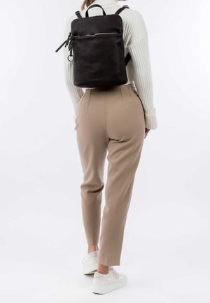 Reppu, joka on valmistettu teksturoidusta mustasta nahasta, suorakaiteen muotoinen, etuosassa vetoketjullinen tasku ja säädettävät hihnat. Yhdistetty beigen värisiin housuihin ja valkoisiin lenkkareihin.