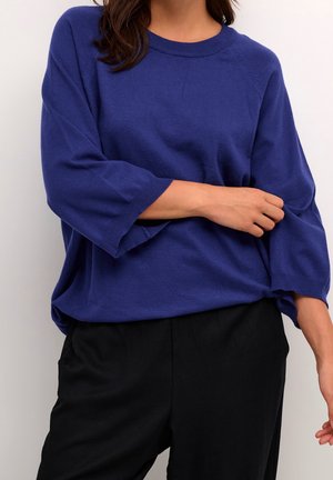 Maglione blu lavorato a maglia con scollo rotondo e maniche a tre quarti, caratterizzato da una vestibilità rilassata e una morbida texture. Abbinato a pantaloni neri.