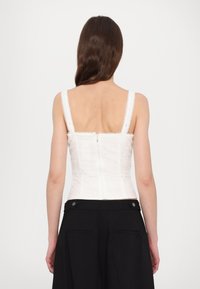 Bustier blanc ajusté avec un design texturé et des fines bretelles, doté d'une fermeture éclair dans le dos, associé à un pantalon noir taille haute.