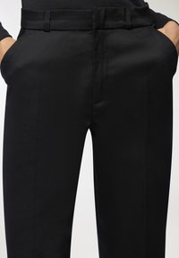 Pantaloni neri su misura realizzati in un tessuto liscio, con una linea frontale piana e tasche laterali, corredati di passanti per cintura per uno stile e una funzionalità ottimali.