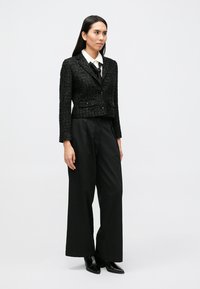 Czarna krótka kurtka z teksturowanej tkaniny z dwoma przednimi kieszeniami i pojedynczym zapięciem na guzik, zestawiona z wysokim stanem czarnych spodni.