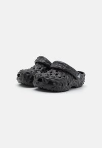 Sabots Crocs noires texturées avec des sangles arrière réglables et des trous de ventilation, présentés sur un fond blanc.