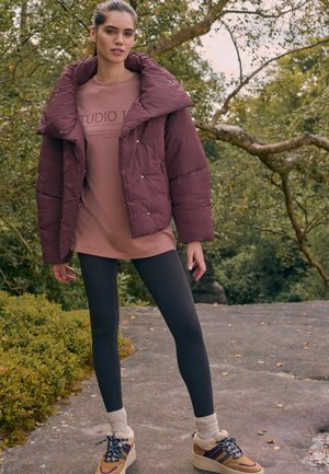 Jachetă puffer marou oversized, tricou grafic bej, colanți negri și pantofi bej cu șosete albe; material texturat și închideri cu capse.