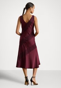 Bordó szatén ruha V-alakú hátkialakítással, csipke díszítéssel átlós csíkokban és bővülő szoknyával. Feket lábfej pántos magassarkúval párosítva.