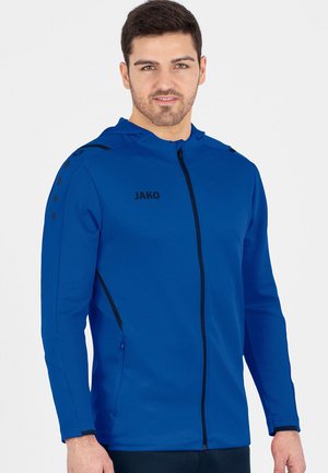 Blaue Zip-Hoodie aus strukturiertem Stoff. Merkmale sind eine Kapuze, schwarze Akzente und das JAKO-Logo. Sie verfügt über seitliche Taschen und ein gepunktetes Schulterdesign.