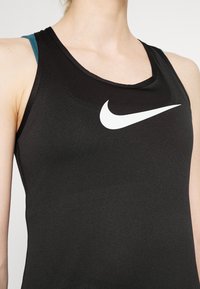 Svart träningslinne med rundad halsringning, med en stor vit Nike swoosh-logotyp på framsidan och turkosa axelband synliga under.
