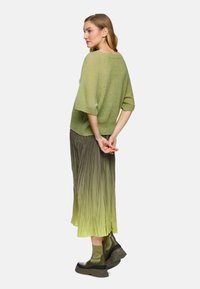 Green knit sweater with short sleeves, paired with a pleated, gradient skirt transitioning from dark green to light green, and chunky green boots.