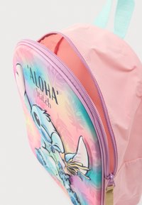 Rožinė vaikų kuprinė su violetine užtrauktuku, mėlynomis petnešomis ir priekyje atspaudu su personažu Stitch bei užrašu „ALOHA Stitch“ ant pastelinio fono.